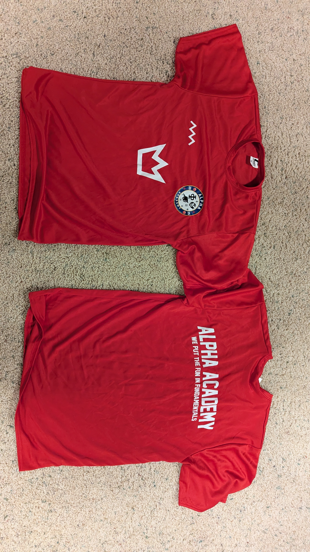 Alpha Academy official red training jersey — front with crest and back with 'We Put the Fun in Fundamentals' wordmark